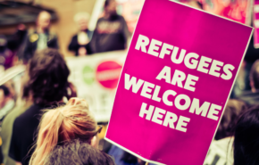 crowd at a protest, person holding sign that says, "refugees are welcome here"