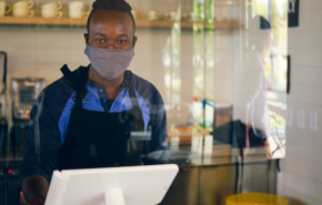 worker in mask stands behind a glass partition at a register