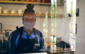 worker in mask stands behind a glass partition at a register