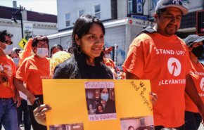 Smiling woman holds sign while walking at a march. Man stands next to her wearing ballcap