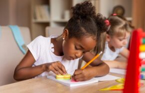 Girl with pigtails sits at desk writing with a pencil