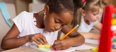 Girl with pigtails sits at desk writing with a pencil
