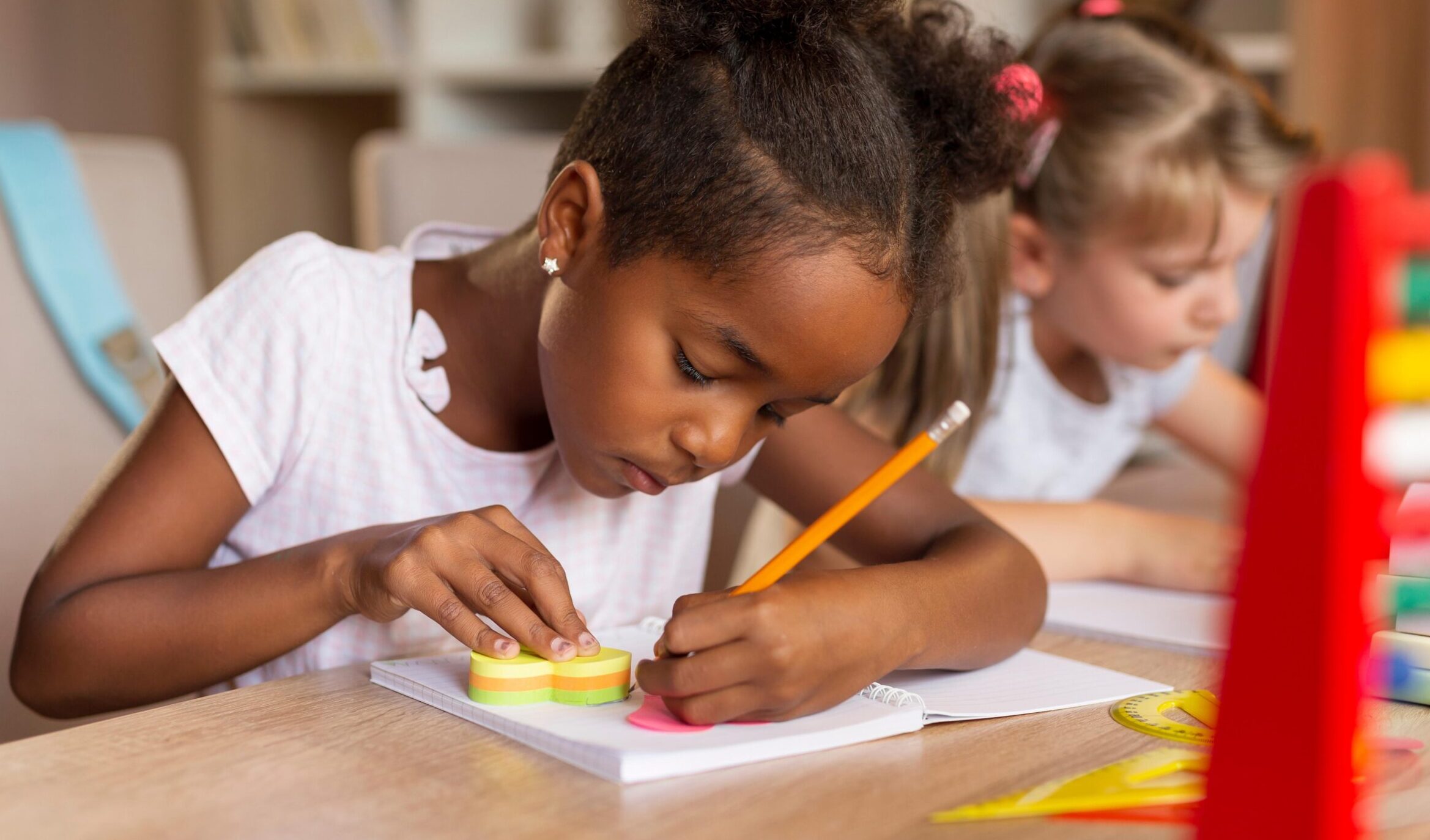 Girl with pigtails sits at desk writing with a pencil