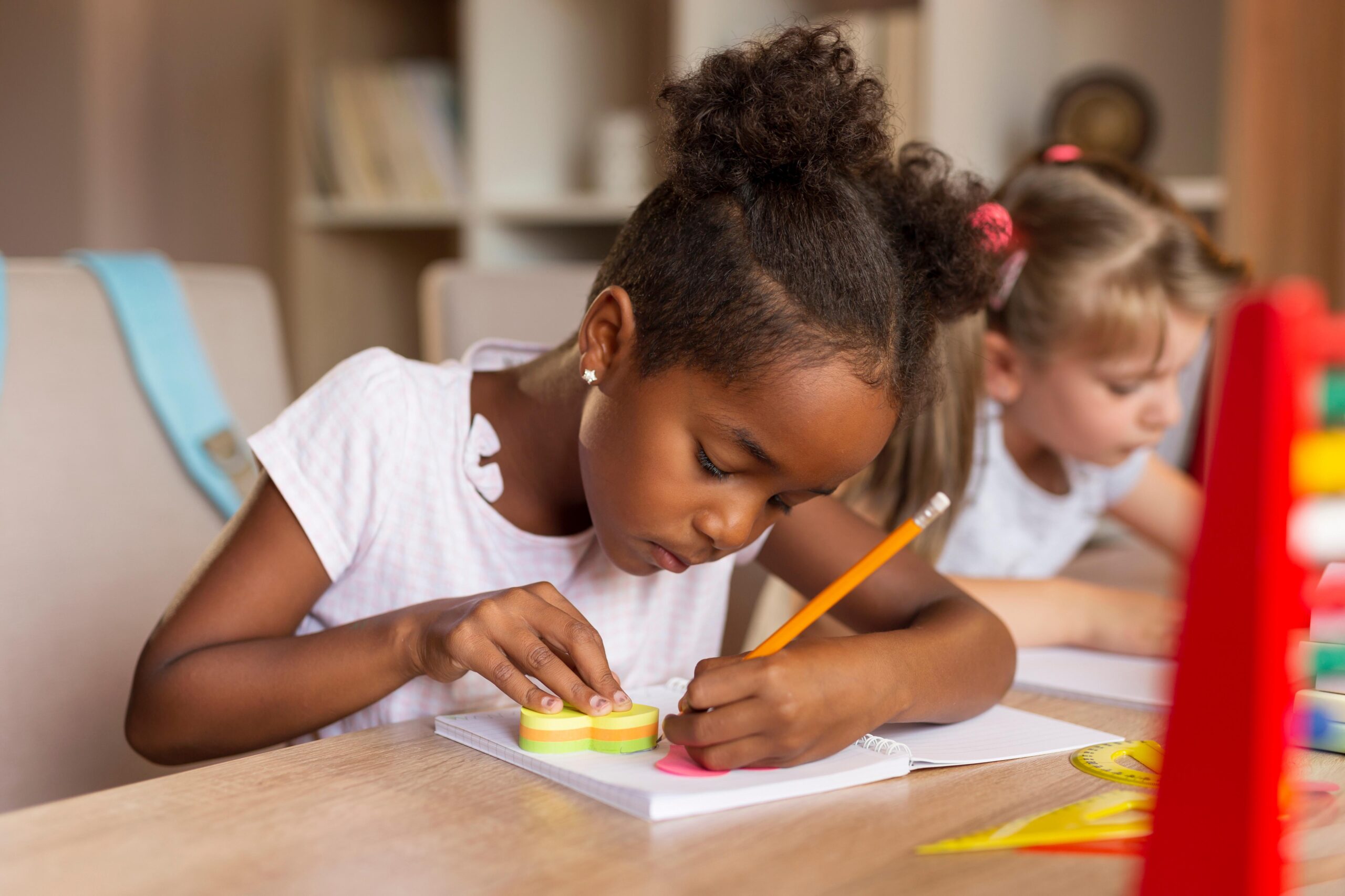 Girl with pigtails sits at desk writing with a pencil