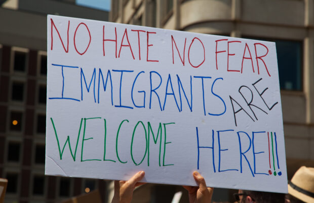 Hands holding up a sign that says "No hate, no fear, immigrants are welcome here"
